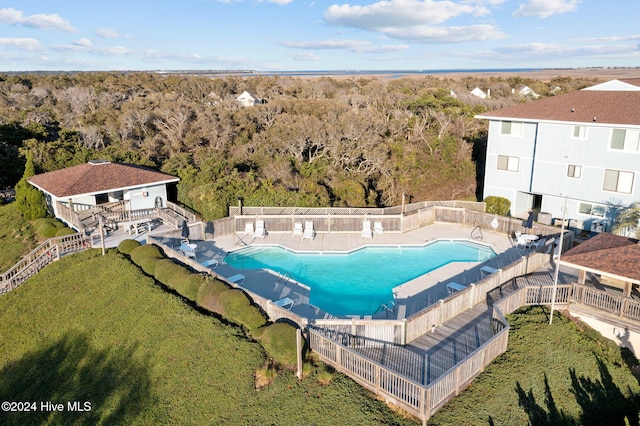 pool with a forest view, a yard, a patio area, and fence