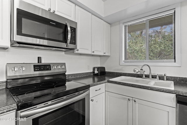 kitchen featuring stainless steel appliances, dark countertops, white cabinetry, and a sink