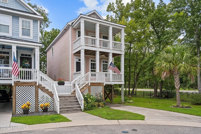 raised beach house featuring a front lawn, fence, concrete driveway, a balcony, and stairs