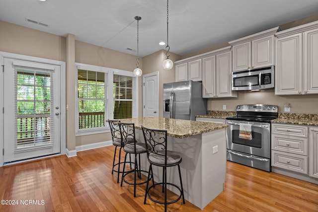 kitchen featuring a center island, light wood-type flooring, light stone counters, a kitchen breakfast bar, and stainless steel appliances