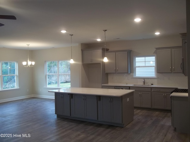 kitchen featuring backsplash, gray cabinetry, a center island, light countertops, and a sink