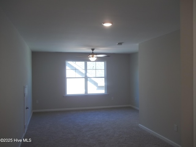 unfurnished room with a ceiling fan, dark colored carpet, and baseboards