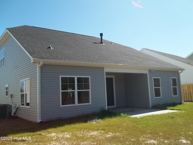 rear view of property featuring a yard, a patio, central AC unit, and a shingled roof