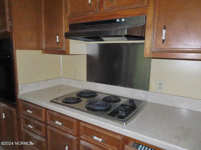 kitchen with brown cabinets, light countertops, stainless steel electric cooktop, oven, and under cabinet range hood