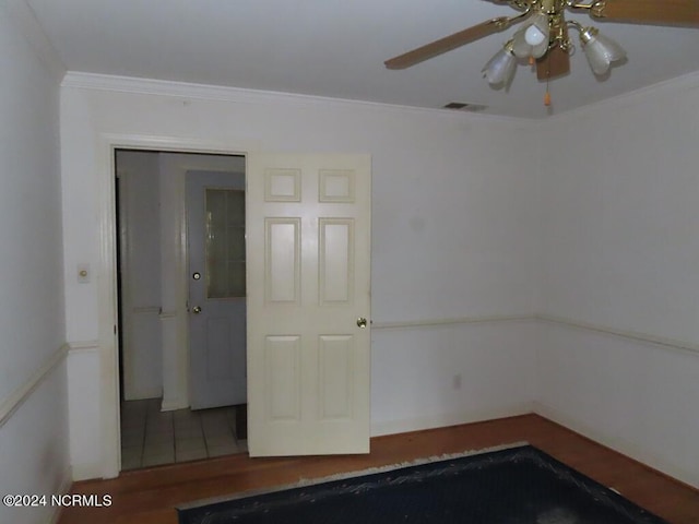 empty room featuring visible vents, wood finished floors, a ceiling fan, and ornamental molding