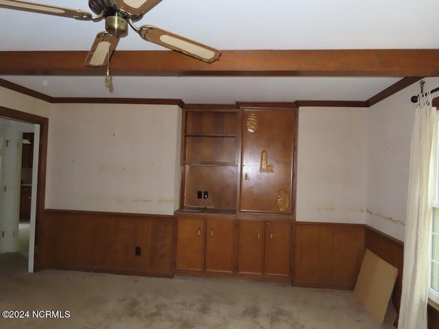 spare room with beam ceiling, light colored carpet, wainscoting, ceiling fan, and wooden walls