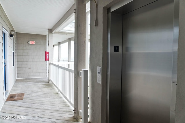 corridor featuring tile walls, light hardwood / wood-style flooring, elevator, and a healthy amount of sunlight