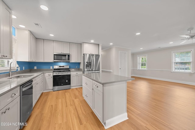 kitchen featuring a kitchen island, stainless steel appliances, sink, white cabinets, and light hardwood / wood-style floors