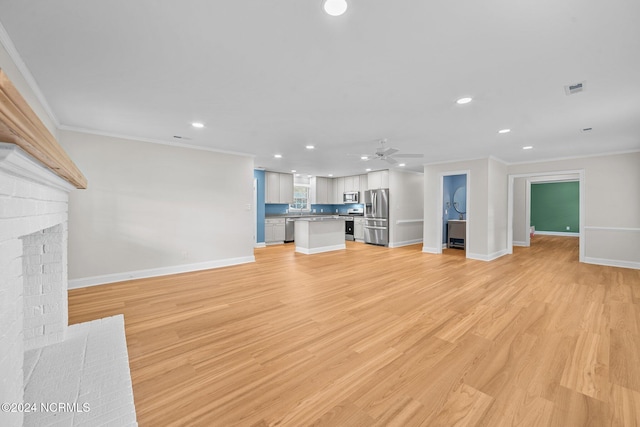 unfurnished living room with light hardwood / wood-style flooring, ornamental molding, ceiling fan, and a brick fireplace