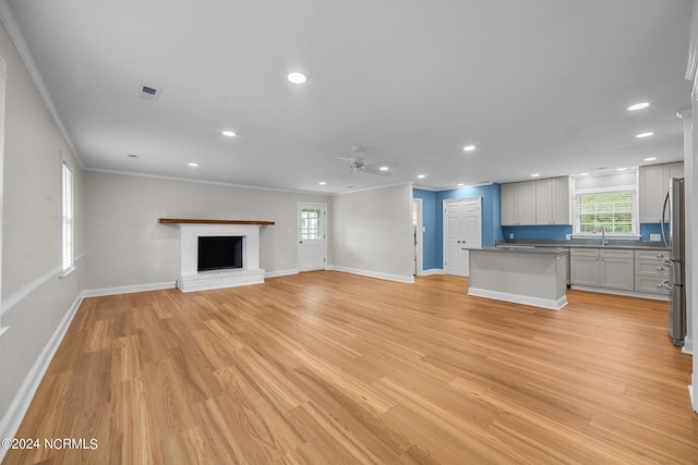 unfurnished living room with light hardwood / wood-style floors, ornamental molding, sink, and a brick fireplace