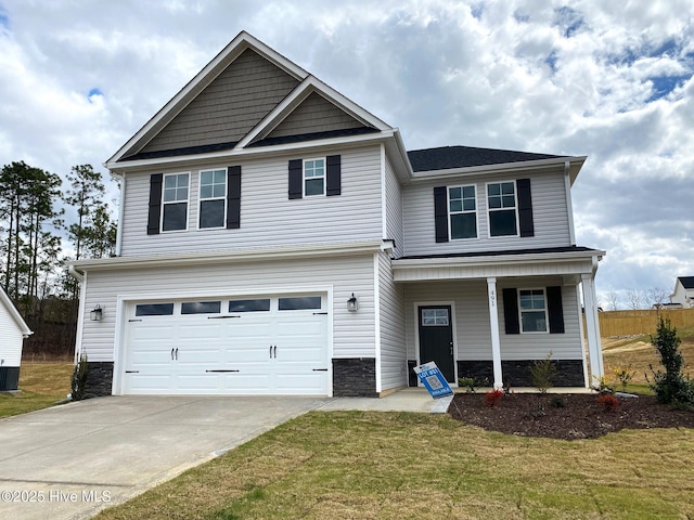 traditional home featuring covered porch, an attached garage, a front yard, stone siding, and driveway