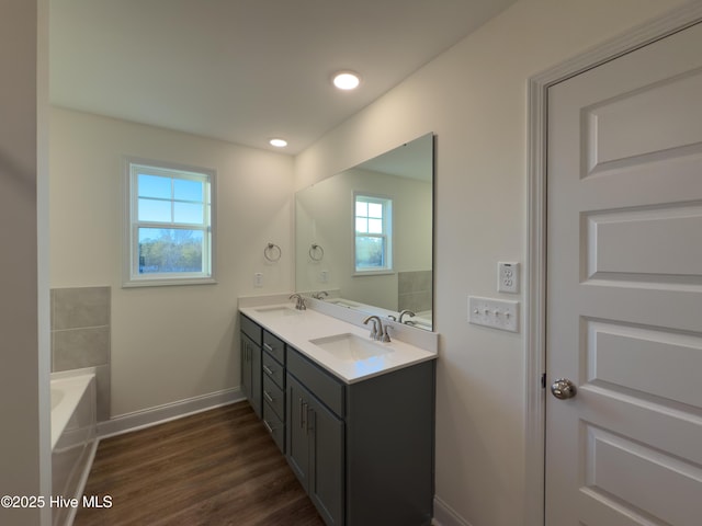 bathroom featuring a sink, a bathing tub, wood finished floors, double vanity, and baseboards