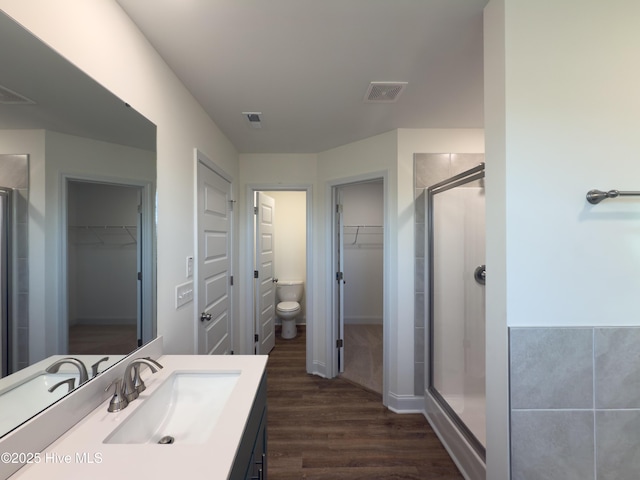 bathroom featuring visible vents, toilet, wood finished floors, a shower stall, and vanity