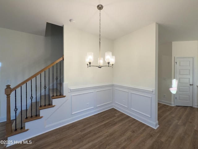 unfurnished dining area featuring a chandelier, a wainscoted wall, dark wood finished floors, and stairs