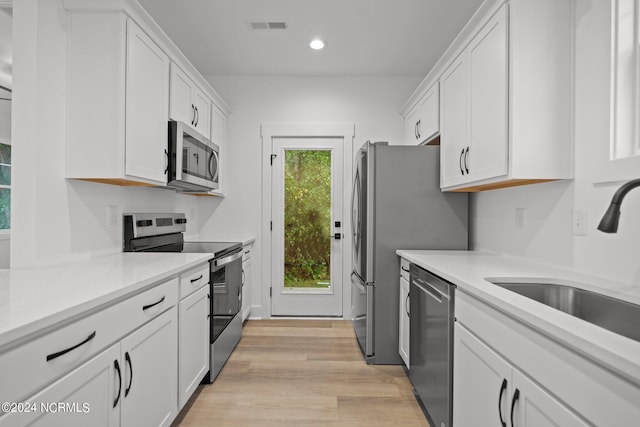 kitchen featuring light stone counters, sink, white cabinetry, stainless steel appliances, and light wood-type flooring