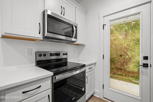 kitchen with light wood-type flooring, white cabinetry, appliances with stainless steel finishes, and a healthy amount of sunlight