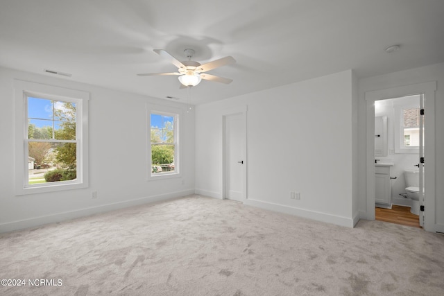 unfurnished bedroom with ceiling fan, light carpet, ensuite bathroom, and multiple windows