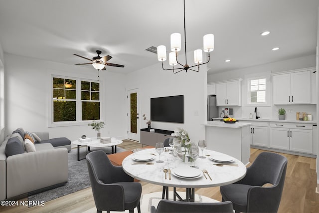 dining area with light hardwood / wood-style flooring, ceiling fan with notable chandelier, and sink