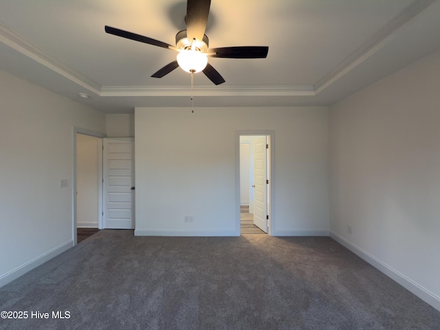 spare room featuring dark colored carpet, ornamental molding, ceiling fan, and a tray ceiling