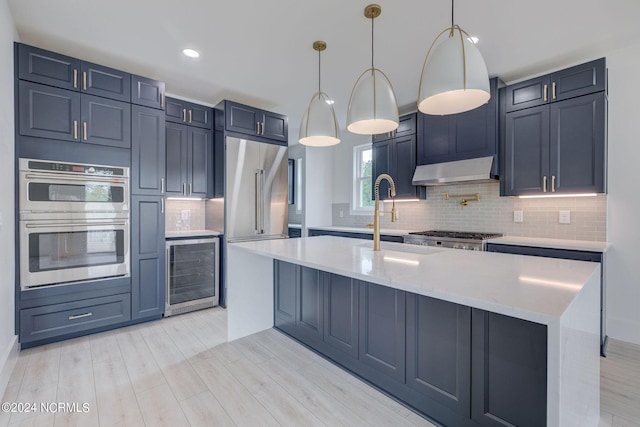 kitchen featuring light stone counters, stainless steel appliances, beverage cooler, pendant lighting, and light hardwood / wood-style floors