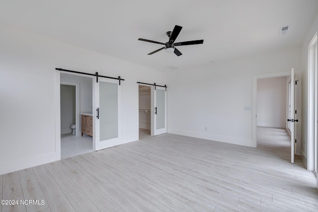 unfurnished bedroom with connected bathroom, a barn door, a walk in closet, and light wood-type flooring