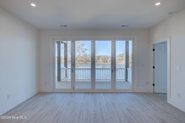 spare room with a water view, light wood-type flooring, and a wealth of natural light