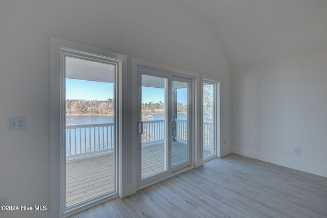 doorway with a water view, vaulted ceiling, and light wood-type flooring