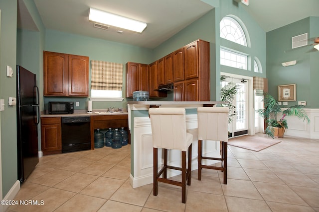 kitchen featuring black appliances, plenty of natural light, a kitchen bar, and light tile patterned floors