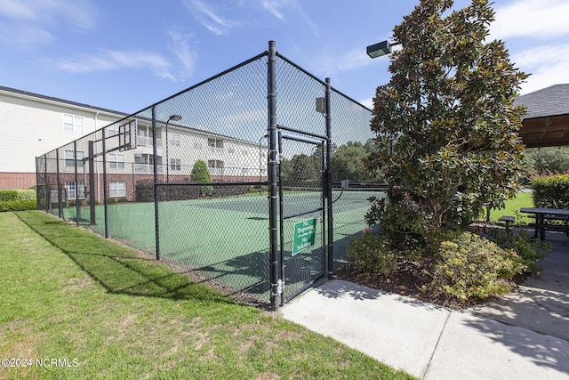 view of tennis court featuring a gate, fence, and a lawn