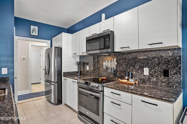 kitchen with dark stone countertops, stainless steel appliances, white cabinets, light tile patterned flooring, and backsplash