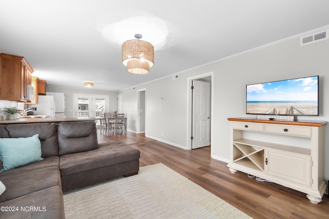 living room featuring dark wood-type flooring, crown molding, sink, and a notable chandelier