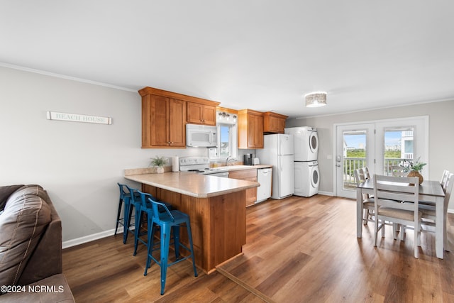 kitchen featuring sink, ornamental molding, stacked washer and clothes dryer, kitchen peninsula, and white appliances