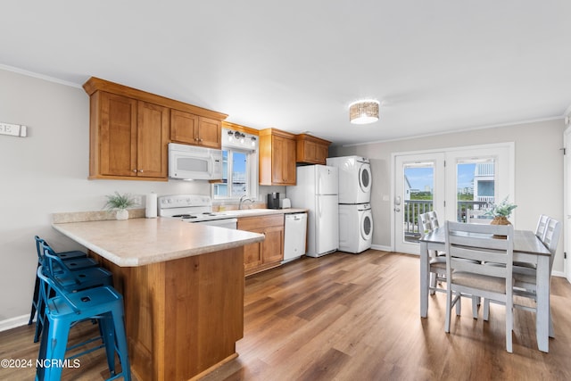 kitchen with stacked washer / dryer, sink, kitchen peninsula, crown molding, and white appliances