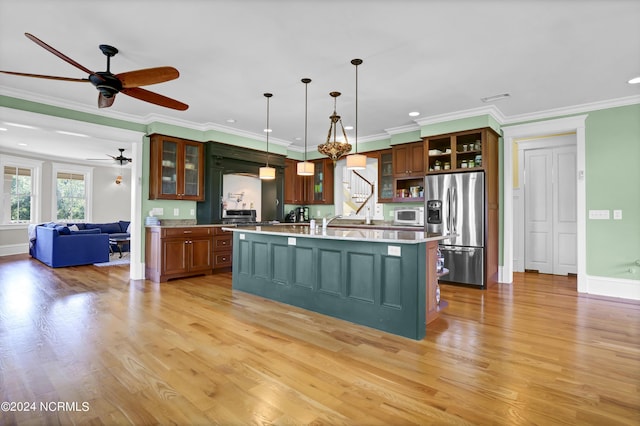 kitchen with a center island with sink, light hardwood / wood-style flooring, crown molding, stainless steel fridge, and ceiling fan