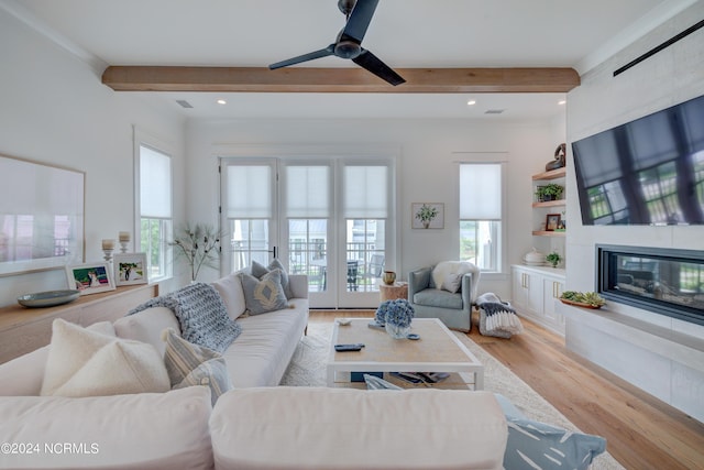 living room featuring light wood-type flooring, a fireplace, visible vents, and beam ceiling