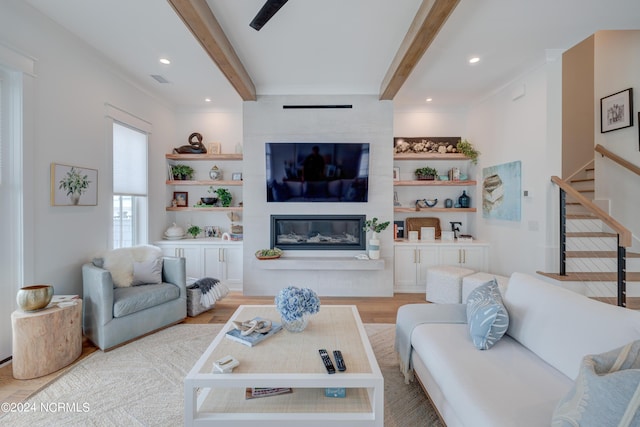 living area with stairway, a fireplace, beamed ceiling, and light wood-style flooring