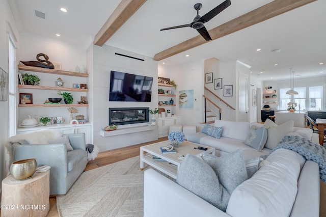 living area with built in shelves, visible vents, a large fireplace, light wood-type flooring, and beamed ceiling