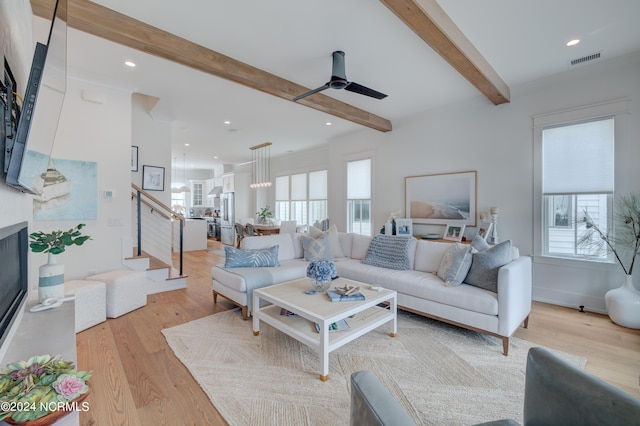 living room with light wood finished floors, visible vents, a glass covered fireplace, beamed ceiling, and stairs