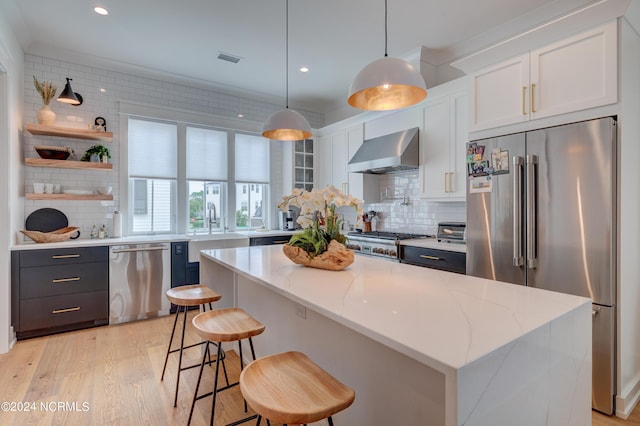 kitchen featuring open shelves, hanging light fixtures, appliances with stainless steel finishes, white cabinets, and wall chimney exhaust hood