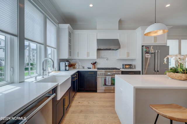 kitchen with decorative light fixtures, white cabinetry, light stone countertops, high quality appliances, and wall chimney exhaust hood