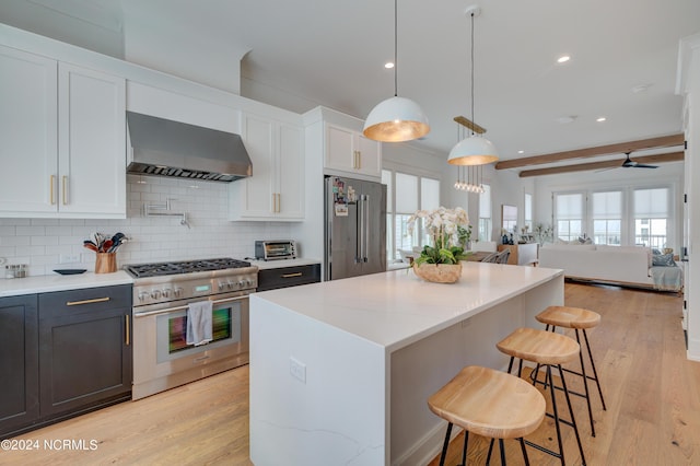 kitchen with premium appliances, hanging light fixtures, open floor plan, white cabinets, and wall chimney exhaust hood