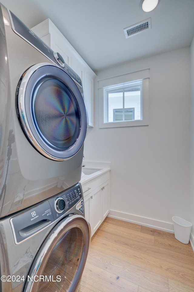 washroom featuring stacked washer and dryer, visible vents, cabinet space, light wood-style flooring, and baseboards