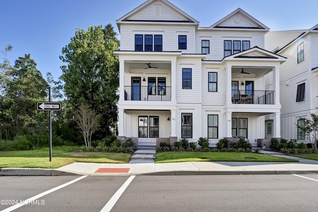 view of property with board and batten siding, a balcony, a ceiling fan, and a front yard