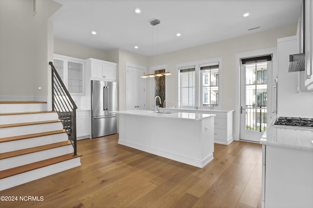 kitchen with pendant lighting, appliances with stainless steel finishes, light wood-style floors, white cabinetry, and an island with sink