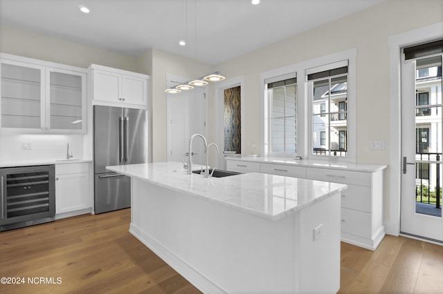 kitchen featuring beverage cooler, high quality fridge, a kitchen island with sink, white cabinetry, and a sink