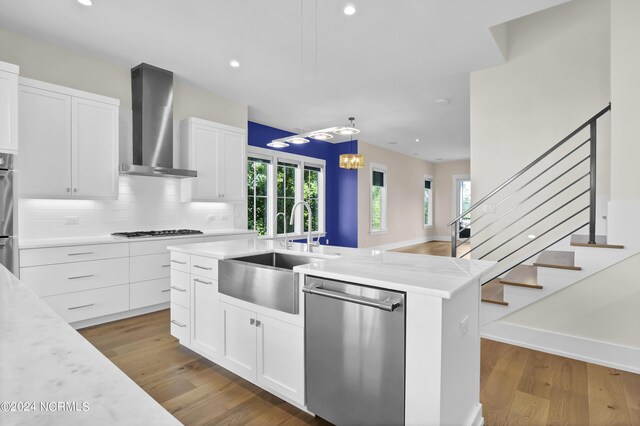 kitchen featuring stainless steel dishwasher, white cabinets, a kitchen island with sink, and wall chimney exhaust hood