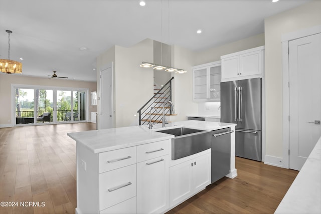 kitchen with appliances with stainless steel finishes, white cabinets, a sink, and a center island with sink