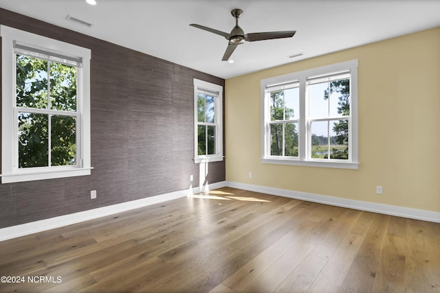 spare room featuring a wealth of natural light, wood finished floors, visible vents, and baseboards