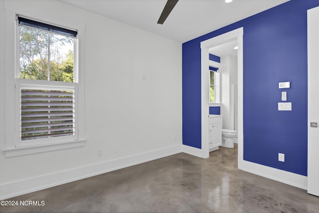 unfurnished bedroom featuring concrete floors, connected bathroom, and baseboards