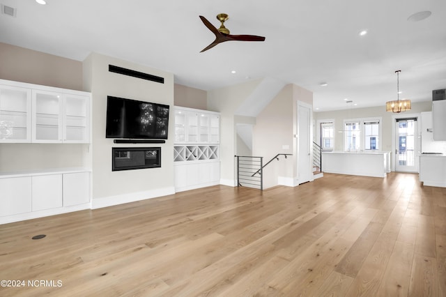 unfurnished living room featuring visible vents, baseboards, light wood-style flooring, stairway, and ceiling fan with notable chandelier